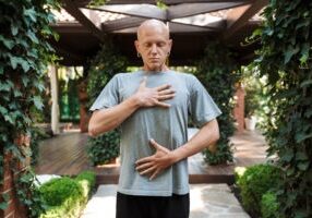 Motivated young fitness man doing breathing exercises while standing outdoors