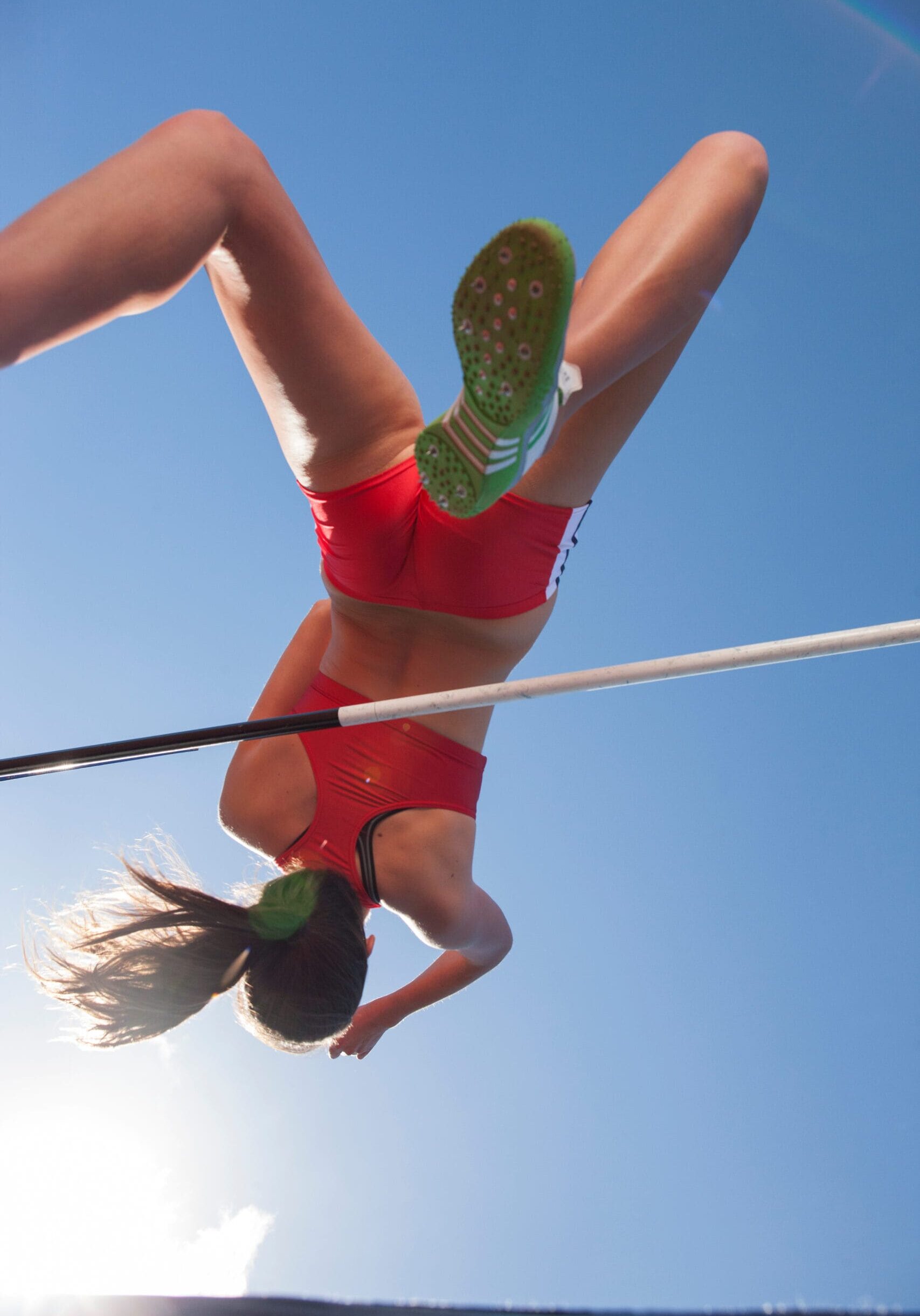 Female track and field athlete high jumping under sunny sky